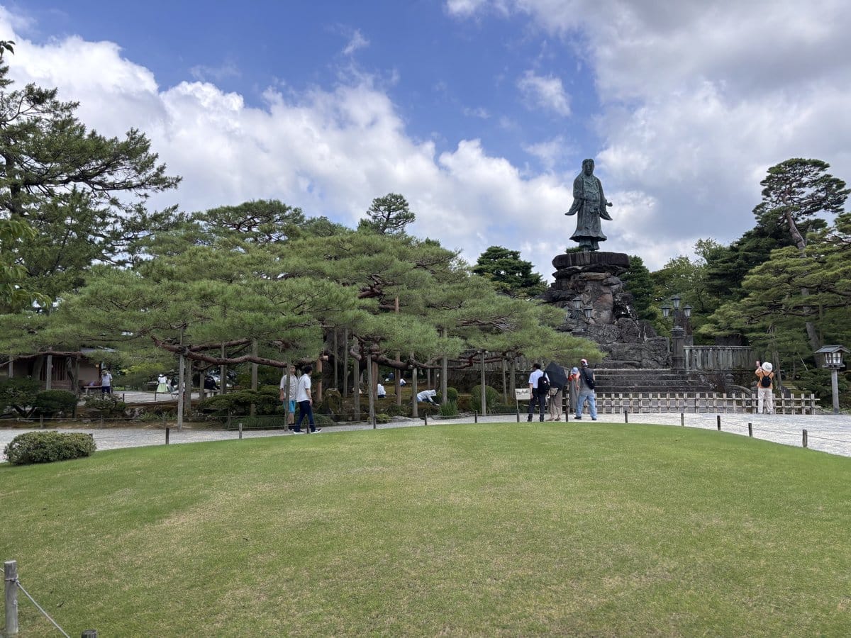 兼六園の芝生広場に立つ明治紀念之標の銅像と石積みの台座