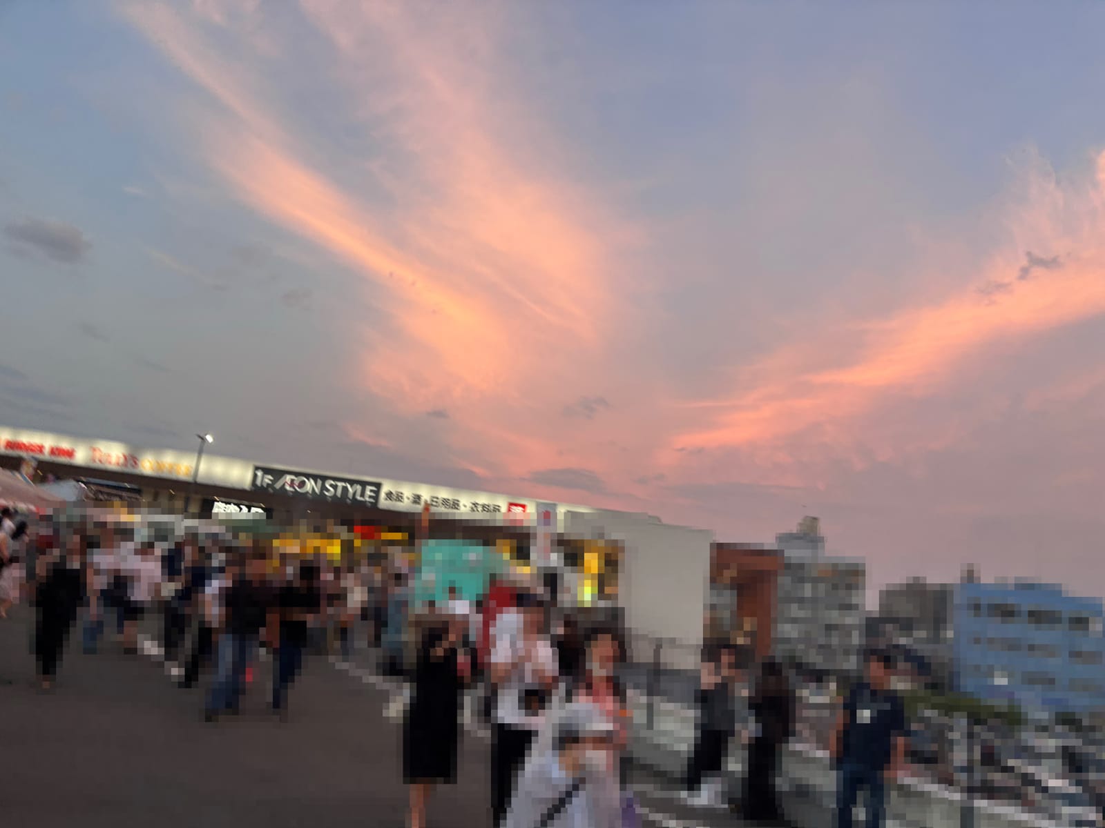 オレンジ色の夕焼け空とイオンスタイルの看板、その前を歩くお祭りの来場者たち