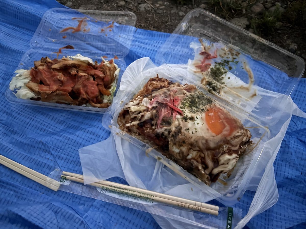 ブルーシートの上に置かれた広島風お好み焼きと、キャベツたっぷりの重ね焼きが入った容器