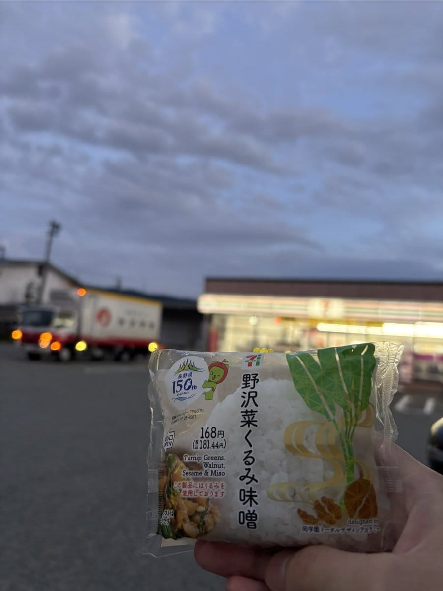 夕方のセブン-イレブン店舗前で手に持った野沢菜くるみ味噌おむすびのパッケージ