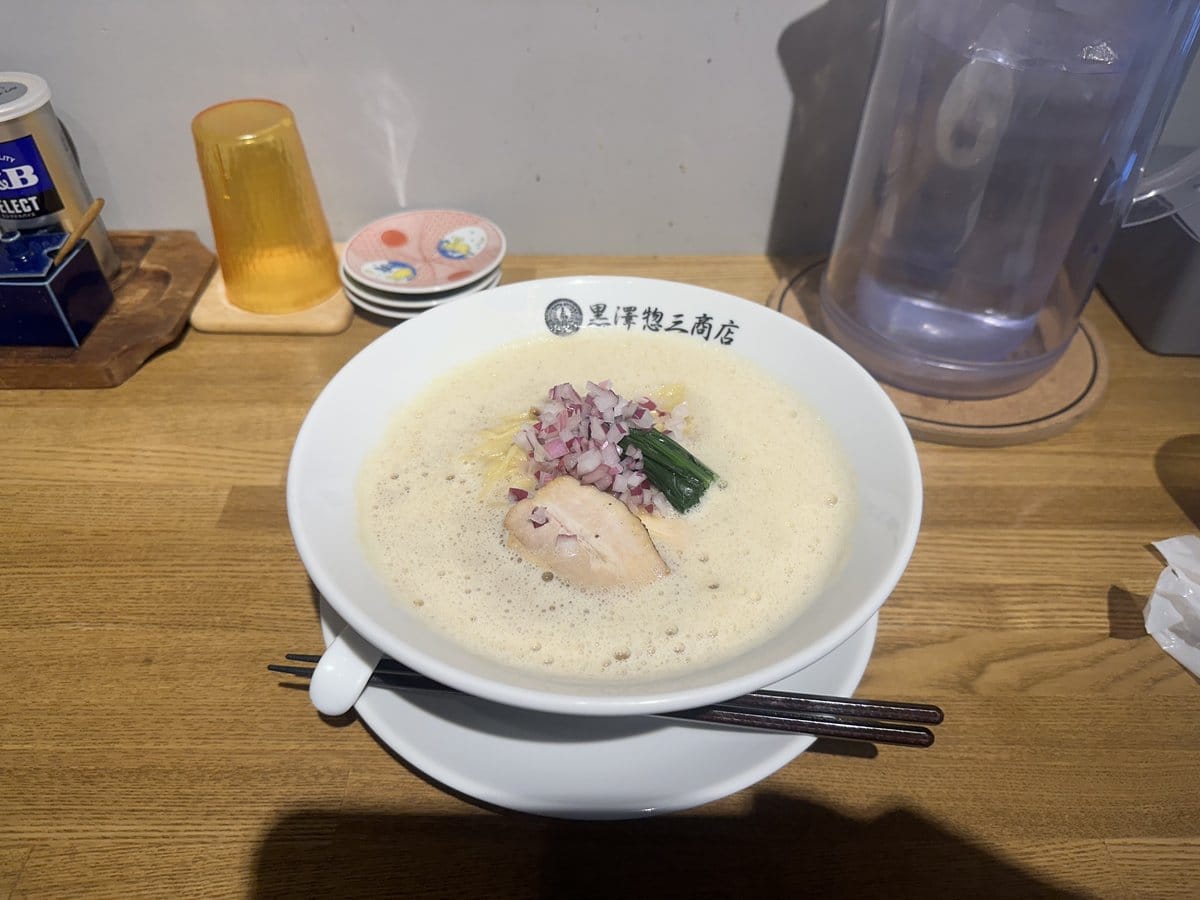 白いどんぶりに入った泡立つ鶏白湯スープ、赤玉ねぎと青菜と鶏叉焼が乗った泡鶏白湯そば